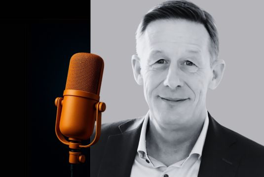 Porträt von Dr. Roger Huber, Arbeits- und Organisationspsychologe, neben einem goldfarbenen Mikrofon – Symbolbild für das Interview im Coopers Executive Blog.