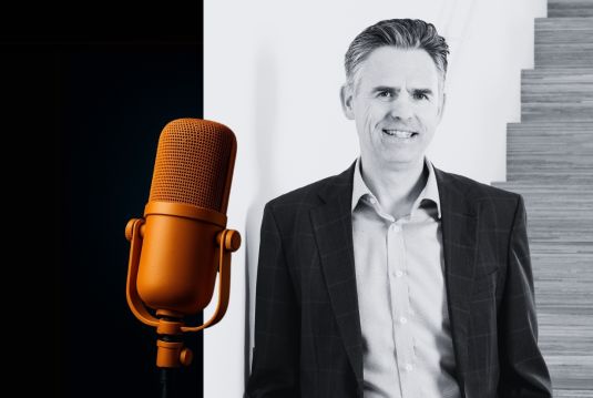 Portrait of Michael Wiendl, Board Member of Coopers Group, smiling with arms crossed next to a microphone.