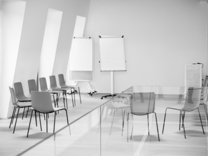 Schwarzweissbild eines modernen Besprechungsraums mit leeren Stühlen und zwei Flipcharts vor heller Wand.