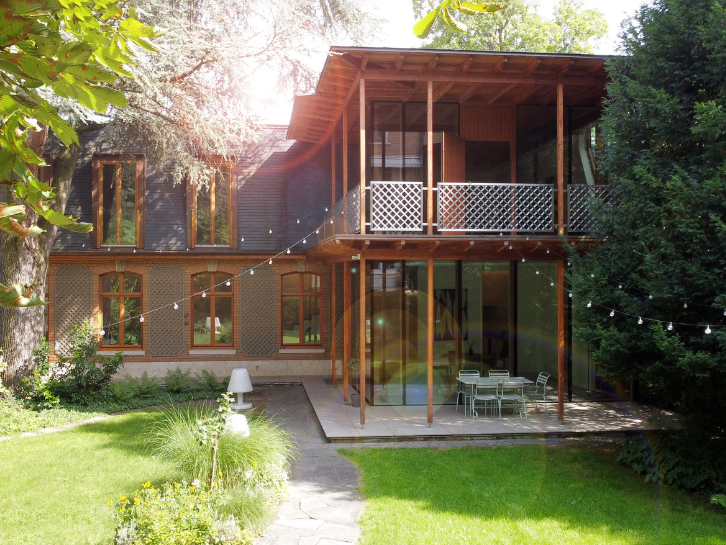 Orangerie | Coopers Group Modern two-storey house with wooden veranda, large windows and garden in the sunlight, surrounded by trees and green space.